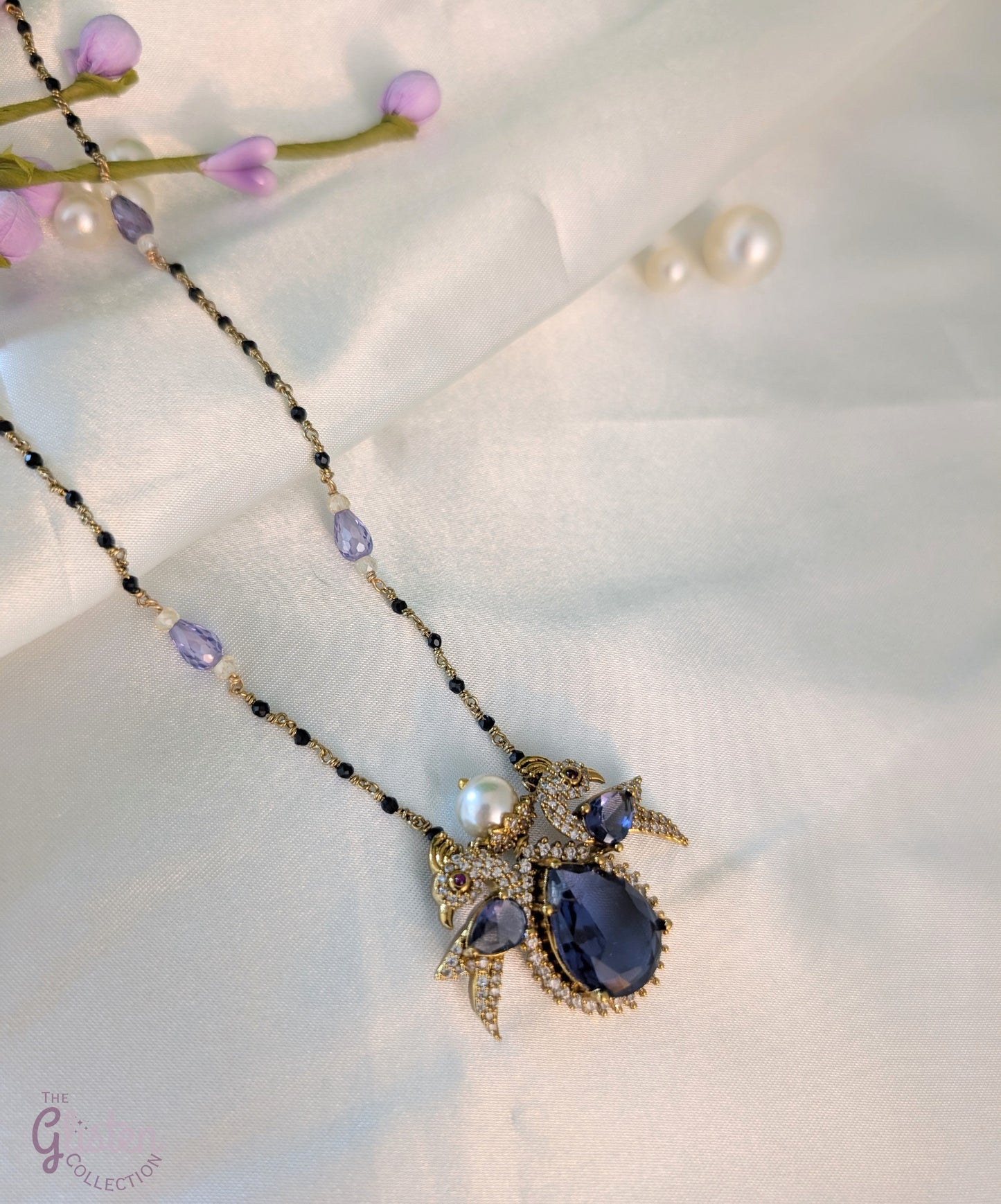 Black bead necklace with sapphire bird pendant, diamond accents, and white pearl — whimsical and elegant design perfect for festive wear.