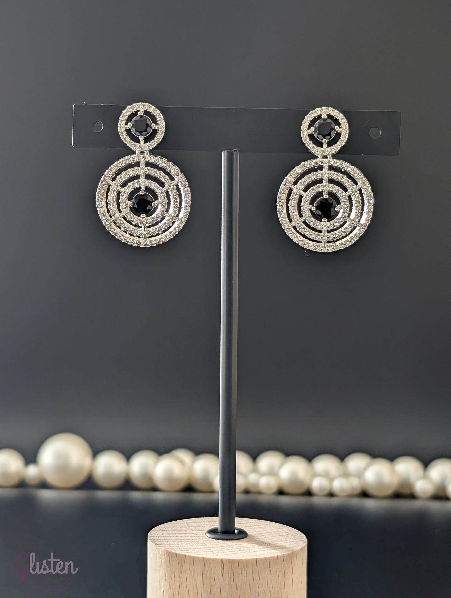 Gold-plated circular drop earrings with sparkling CZ stones and a bold black center stone from The Glisten Collection.