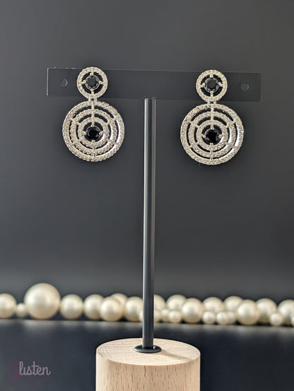 Gold-plated circular drop earrings with sparkling CZ stones and a bold black center stone from The Glisten Collection.