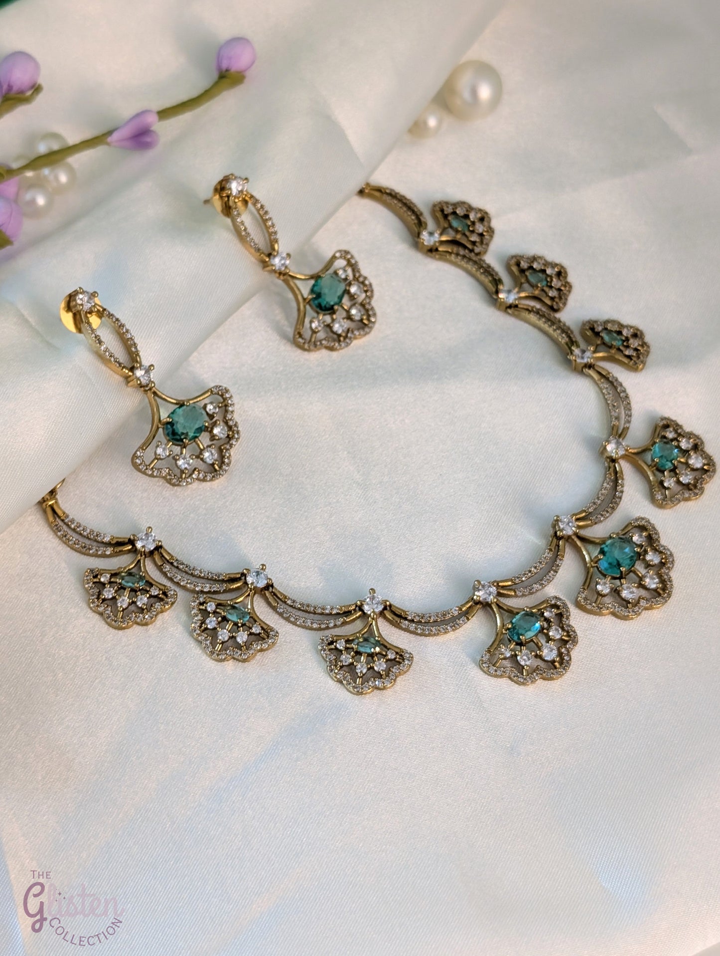 Gold-toned necklace and earrings set with greenish-blue teardrop stones and leaf design, displayed on a white background — perfect for party or special occasion wear.