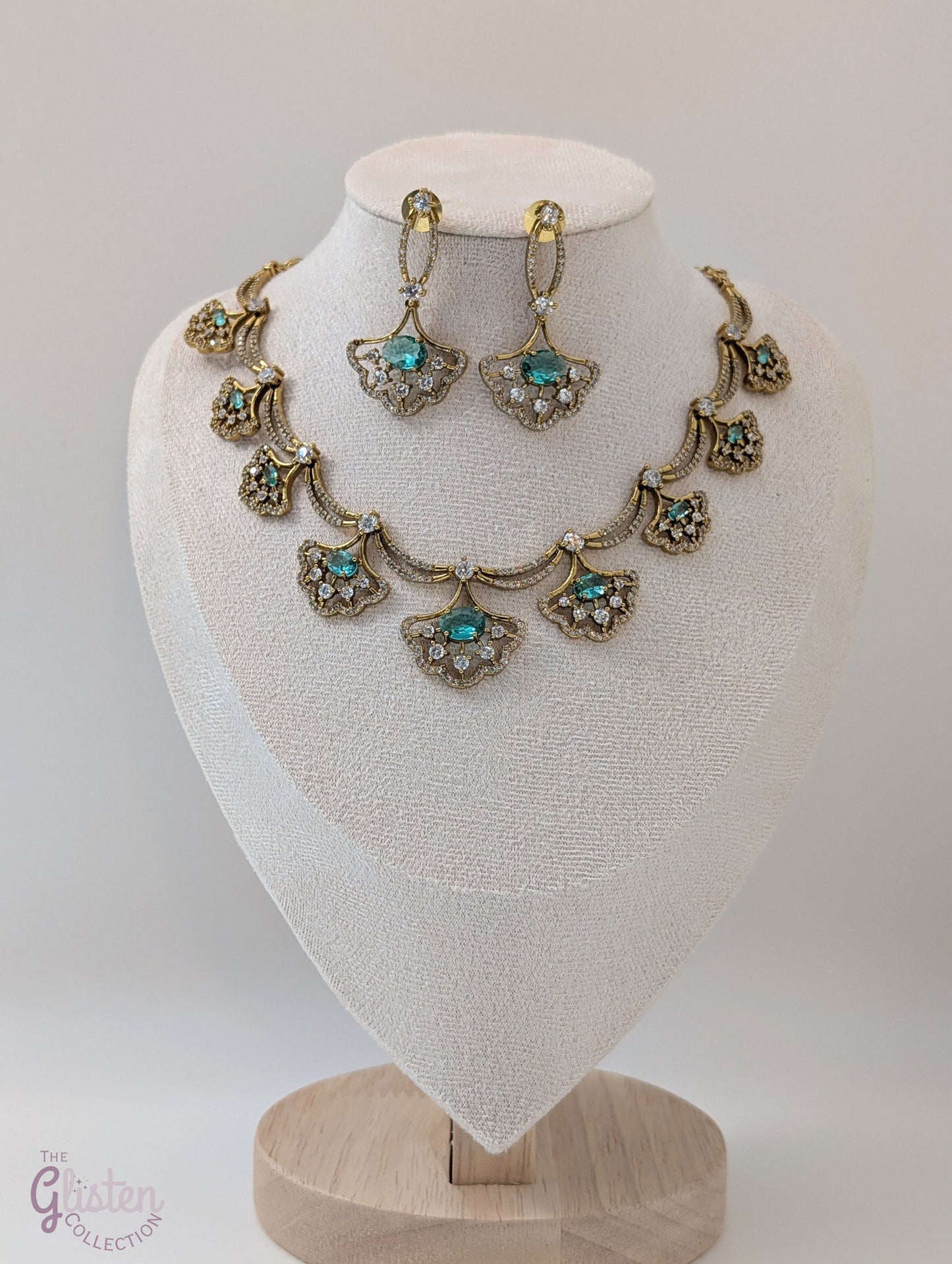 Gold-toned necklace and earrings set with greenish-blue teardrop stones and leaf design, displayed on a white background — perfect for party or special occasion wear.