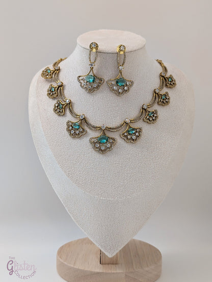 Gold-toned necklace and earrings set with greenish-blue teardrop stones and leaf design, displayed on a white background — perfect for party or special occasion wear.