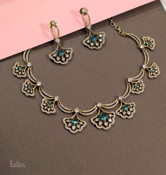 Gold-toned necklace and earrings set with greenish-blue teardrop stones and leaf design, displayed on a white background — perfect for party or special occasion wear.