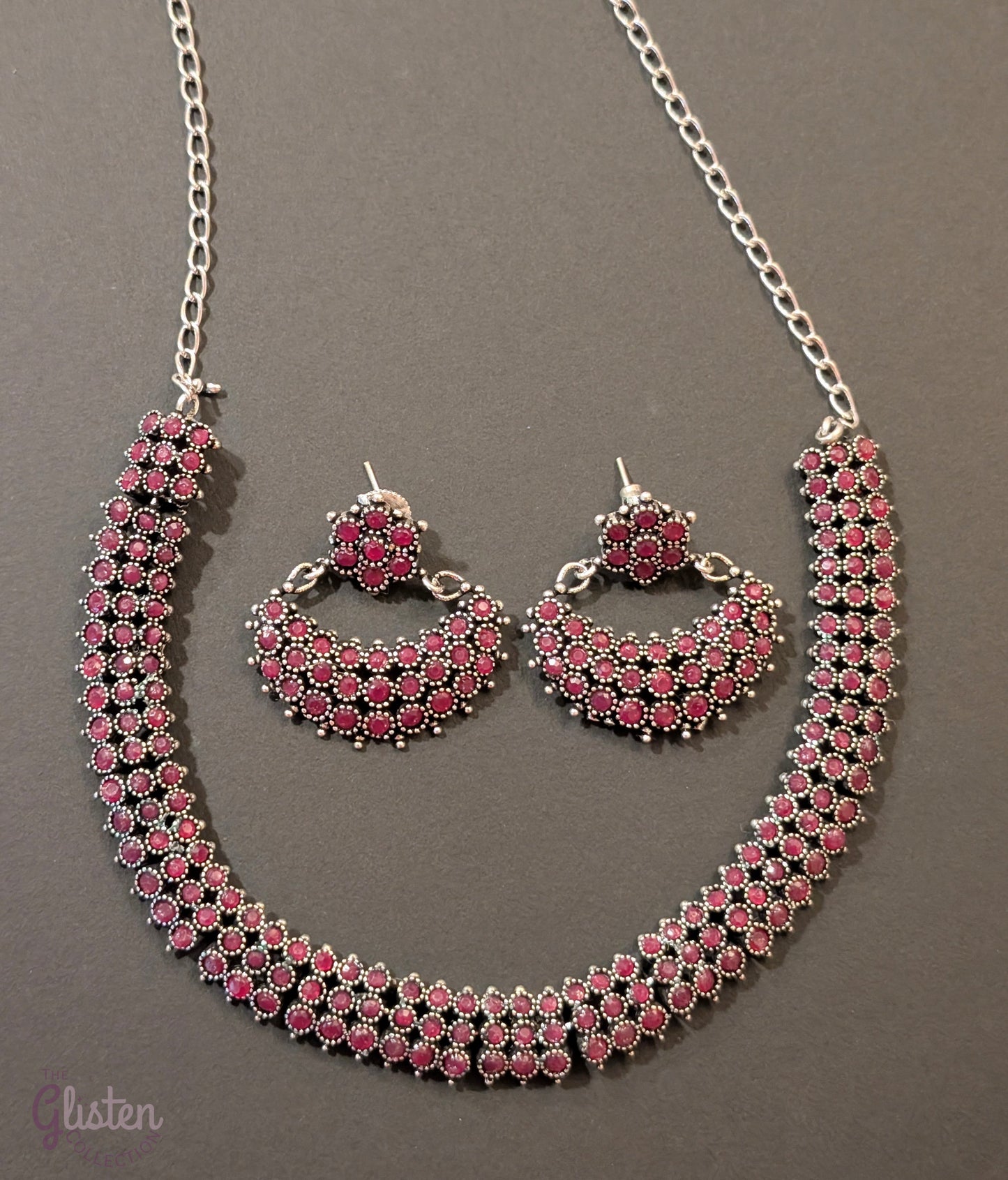 Oxidized silver necklace set with red stones and black finish, paired with crescent-shaped floral earrings — ideal for festive occasions and traditional Indian outfits.