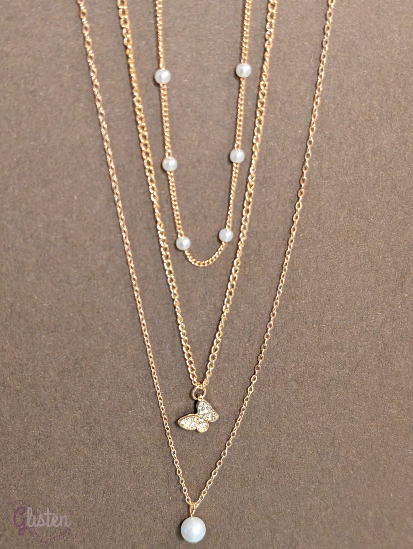 Three-layer gold necklace set with butterfly charm, pearl line, and single pearl pendant; can be worn individually or layered for a stylish statement.