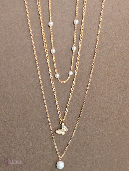 Three-layer gold necklace set with butterfly charm, pearl line, and single pearl pendant; can be worn individually or layered for a stylish statement.