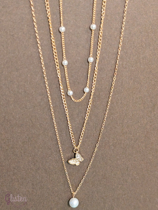 Three-layer gold necklace set with butterfly charm, pearl line, and single pearl pendant; can be worn individually or layered for a stylish statement.