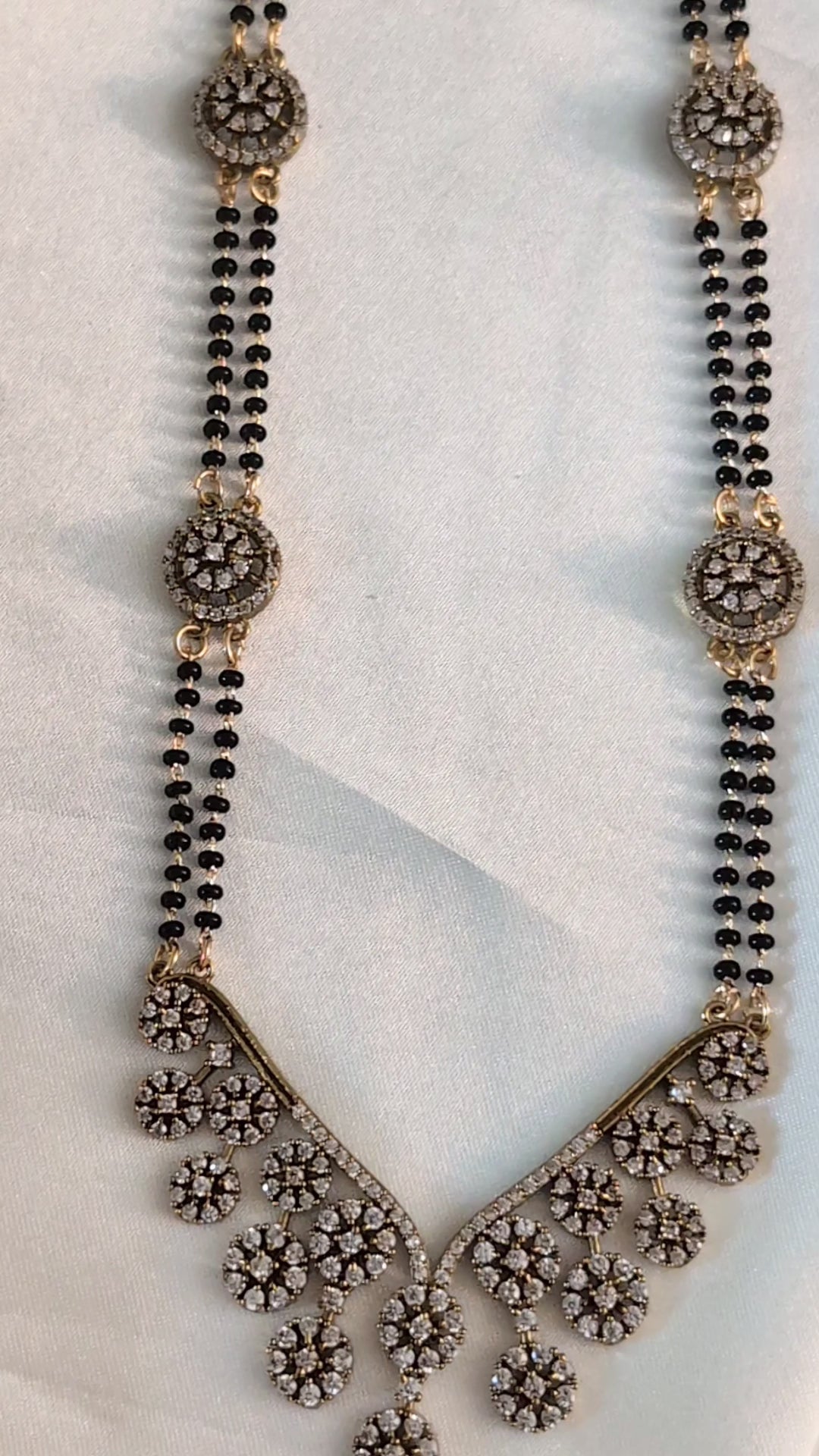 Long mangalsutra with black beads, V-shaped stone pendant, and round stone accents — ideal for modern traditional wear and daily elegance.